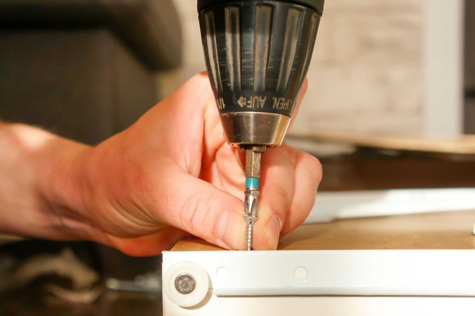 A person operating a drill to secure a screw into a piece of furniture during assembly.