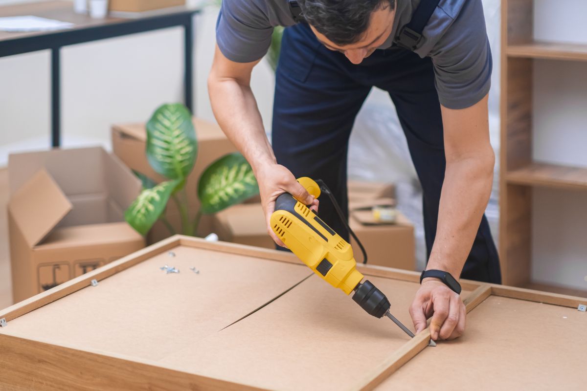 A man uses a drill to construct furniture, showcasing his skills in a furniture repair service.