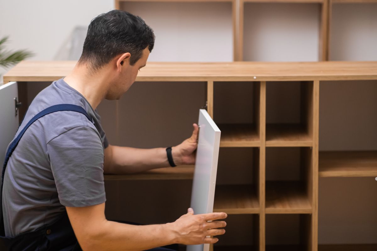 A man inserts a piece of wood into a cabinet as part of a furniture repair service.